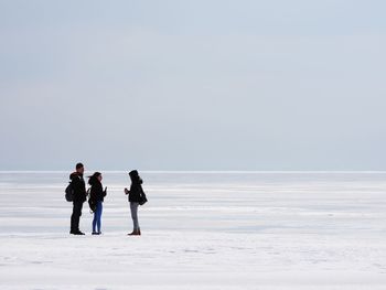 Rear view of people on sea shore against sky during winter