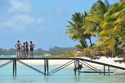 Full length rear view of shirtless friends standing on pier over sea against sky