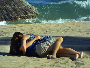 Close-up of romantic couple lying at beach by sea