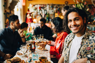 Portrait of smiling young man sitting with multi-ethnic friends enjoying dinner party at restaurant