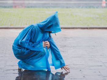 Side view of woman wearing blue raincoat touching wet street during rainfall