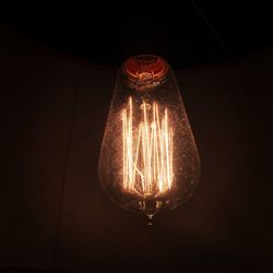 Low angle view of illuminated light bulb hanging against black background