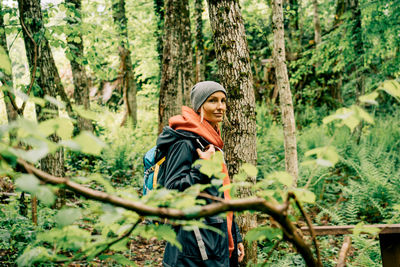 A young caucasian woman in a raincoat and a hat walks along a path in the thickets of the forest