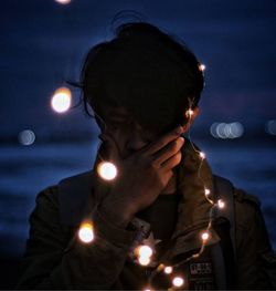 Portrait of young man holding illuminated lighting equipment at night