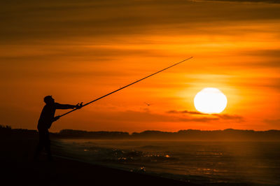 Silhouette man fishing at sunset