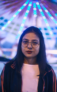 Portrait of young woman standing against illuminated ride