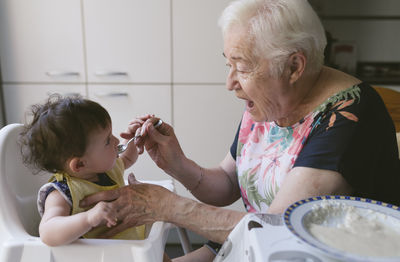 Grandmother feeding baby girl in the kitchen