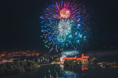 Firework display over illuminated city against sky at night