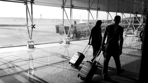 Rear view of people walking with trolleys  at airport