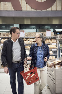 Mature couple talking while walking with basket at supermarket