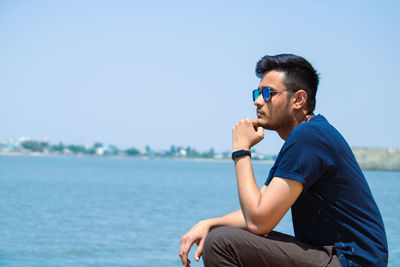 Young man sitting in sea against sky