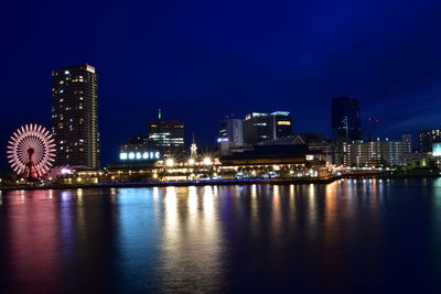 Illuminated buildings by river against sky at night