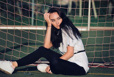 Side view of young woman looking away while sitting by net