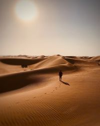 Rear view of silhouette man walking at desert against sky during sunny day