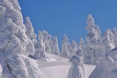 Low angle view of snow covered trees against clear blue sky