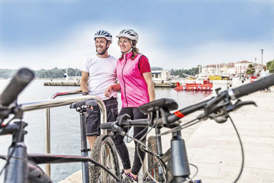 Portrait of happy couple standing by bicycles against sky