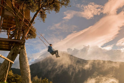 Low angle view of man hanging on tree against sky