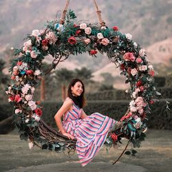 Smiling woman sitting on swing covered in flowers 