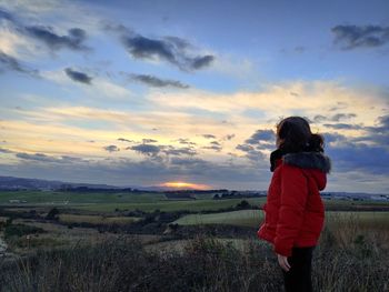 Rear view of woman standing on field against sunset sky