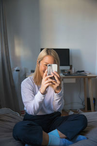 A young woman playing with a smart phone on a bed