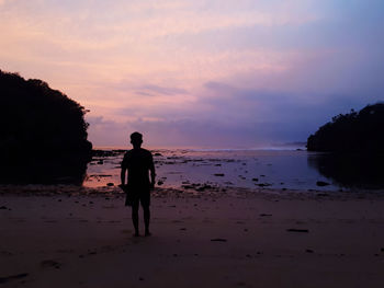 Silhouette man standing on beach against sky during sunset