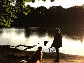 Rear view of silhouette boy standing by lake against sky during sunset