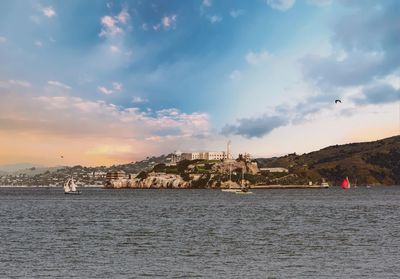 City buildings at waterfront against cloudy sky