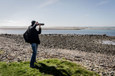 Full length of woman photographing on beach against sky