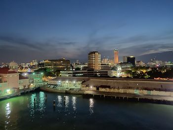 Illuminated buildings by river against sky at night