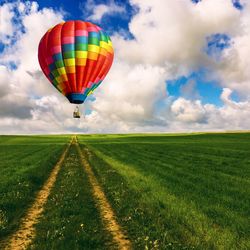 Hot air balloon over grassy field against cloudy sky