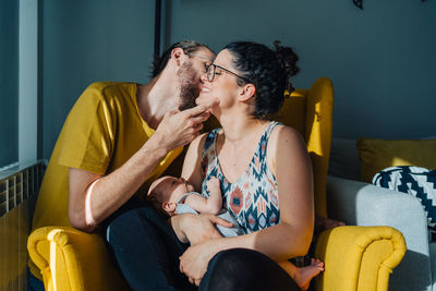 Woman sitting on yellow sofa at home holding her new born baby