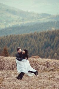 Man carrying woman on field against mountains