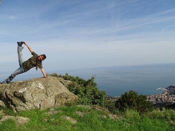 Woman doing yoga on rock by sea against sky