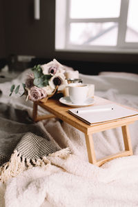 Wooden coffee table with flowers on bed with plaid, coffee cup. lilac roses. interior gray tones