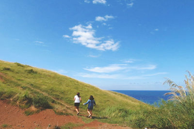 Rear view of people walking on landscape against blue sky