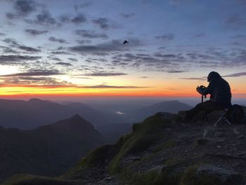 Man on rock against sky during sunset