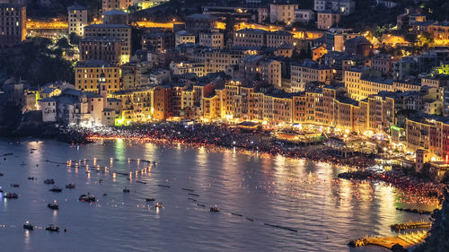 High angle view of illuminated city by sea at night