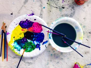 High angle view of paintbrushes by multi colored paints on plate in workshop