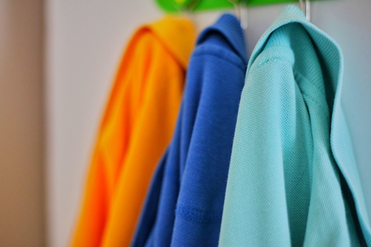 CLOSE-UP OF MULTI COLORED CLOTHES HANGING ON BLUE WALL