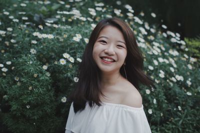 Portrait of smiling young woman standing against flowers at park