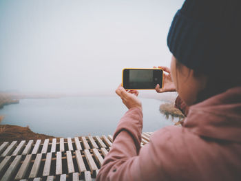 Midsection of man using mobile phone against sea