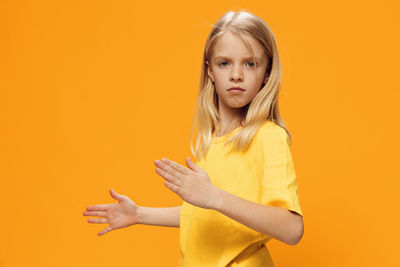 Portrait of young woman with arms raised against yellow background