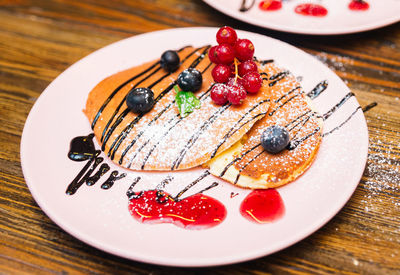 Pink plate with puffed pancakes with currants, blueberries, with powdered sugar, chocolate sauce