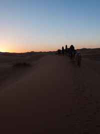 People walking on sand dune against clear sky