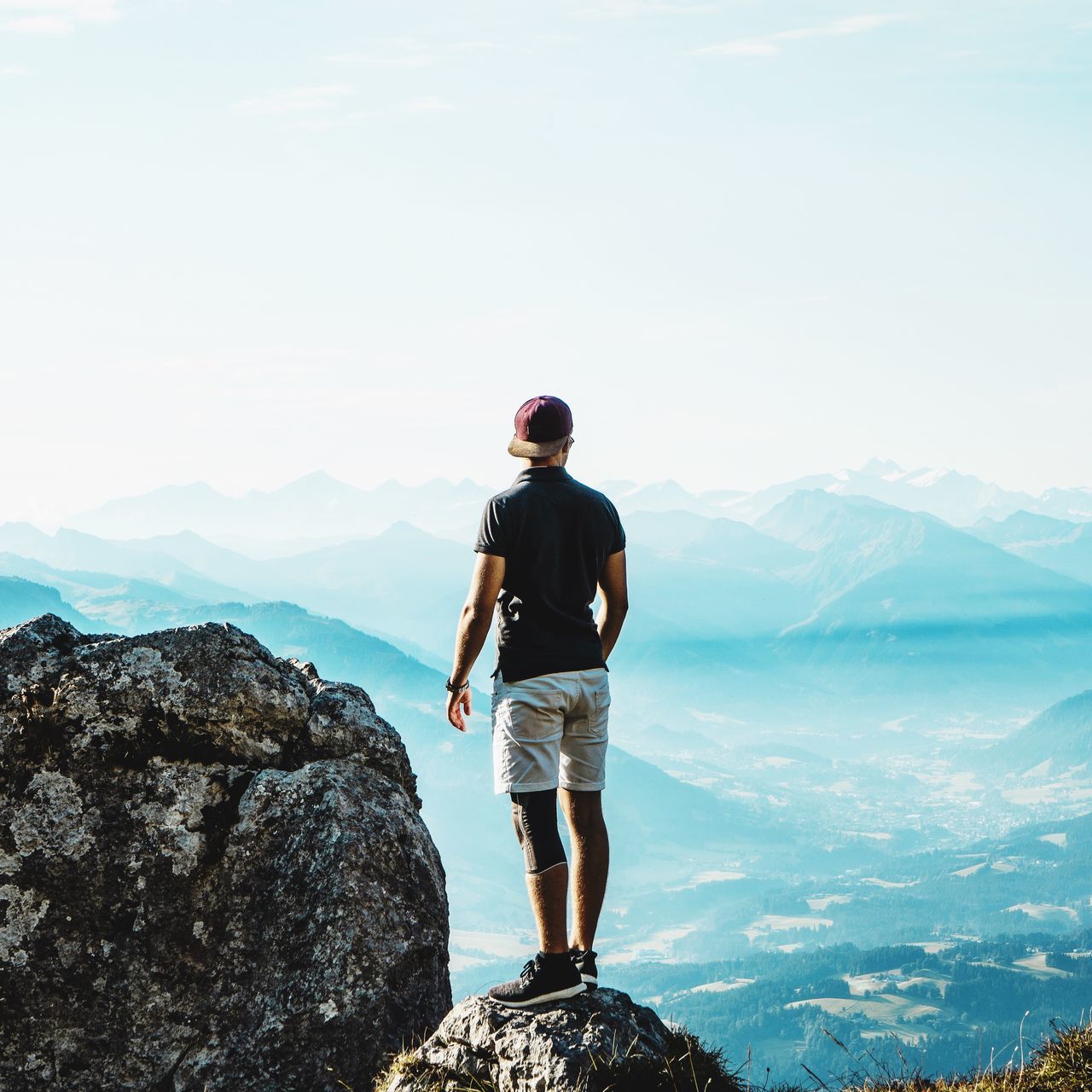 REAR VIEW OF MAN STANDING ON ROCKS AGAINST MOUNTAIN