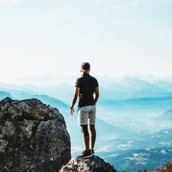 Rear view of man standing on rock looking at mountains