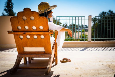 Man sitting on chair by railing against sky