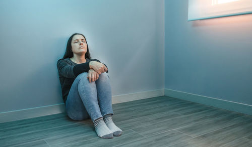 Depressed woman sitting by wall at home