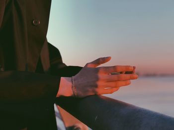 Midsection of man standing by railing against sky during sunset