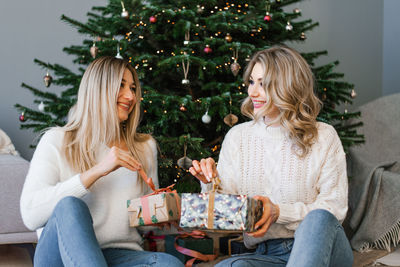 Two happy young girls laugh, friends give each other gifts during the christmas holiday